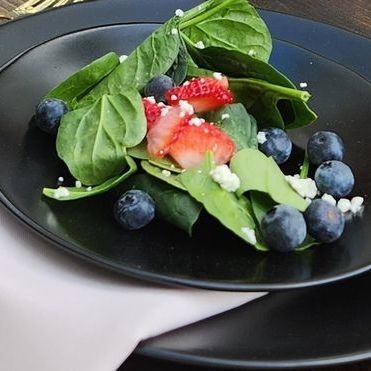 A black plate topped with spinach blueberries and strawberries