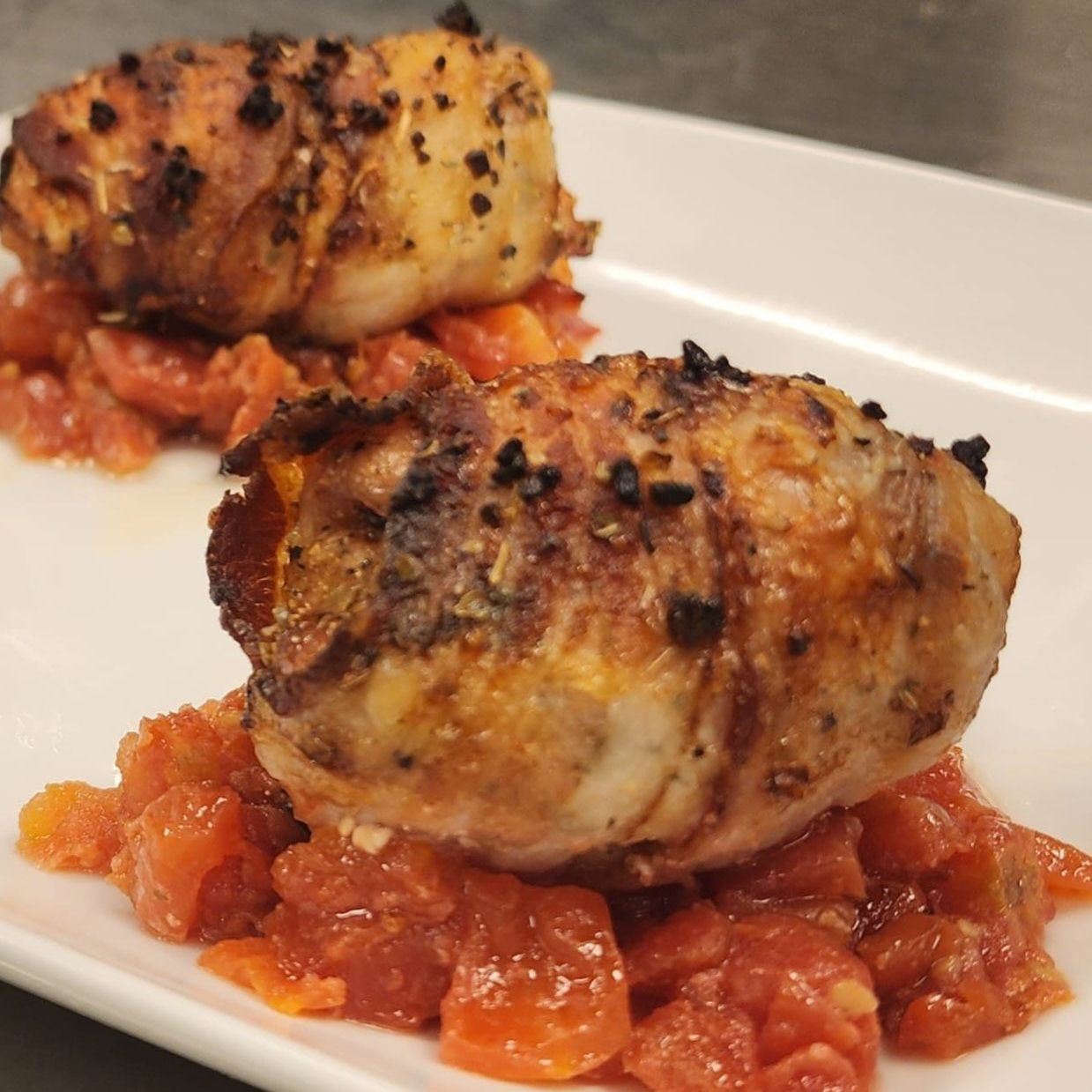 Two pieces of meat on a white plate with tomato sauce