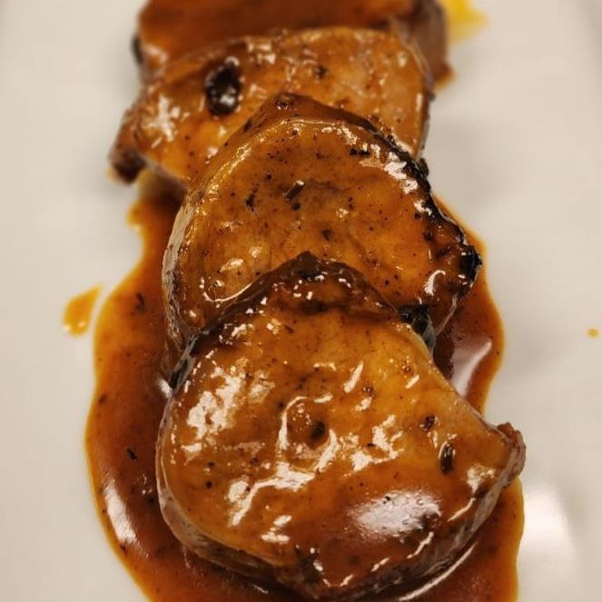 A white plate topped with slices of meat and sauce