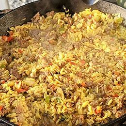 A pan filled with rice, meat, and vegetables is being cooked on a stove.