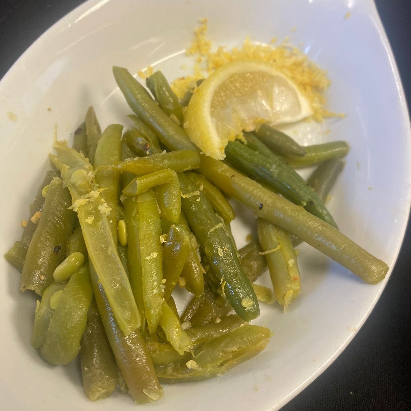 A white plate topped with green beans and a slice of lemon.