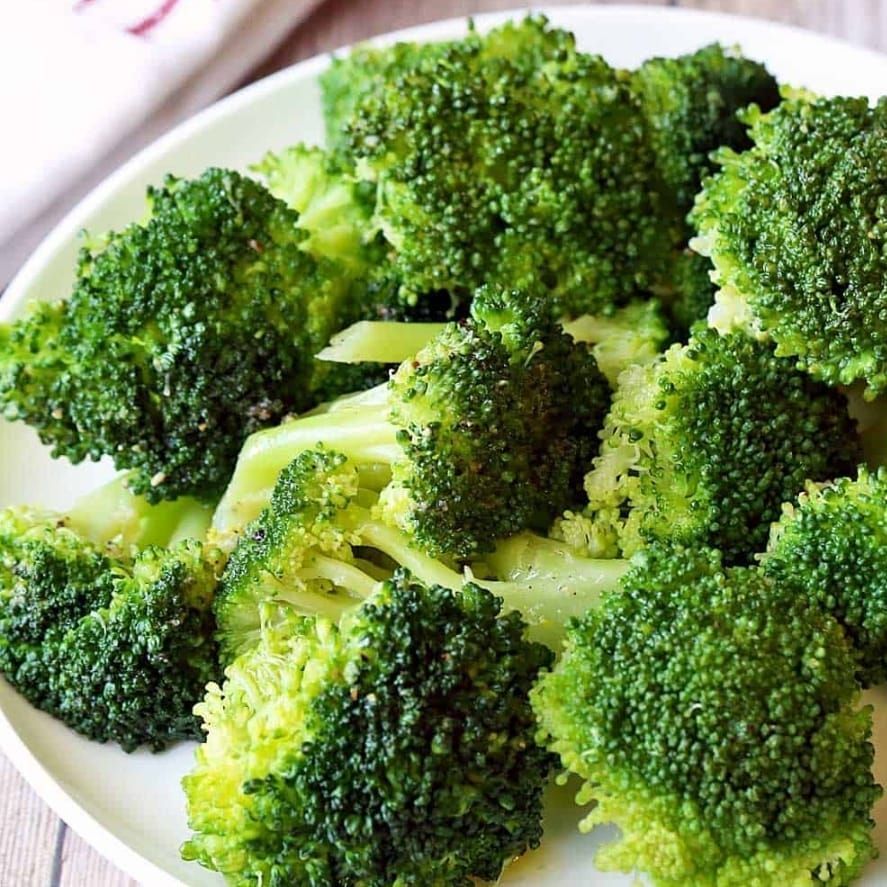 A white plate topped with broccoli on a wooden table.