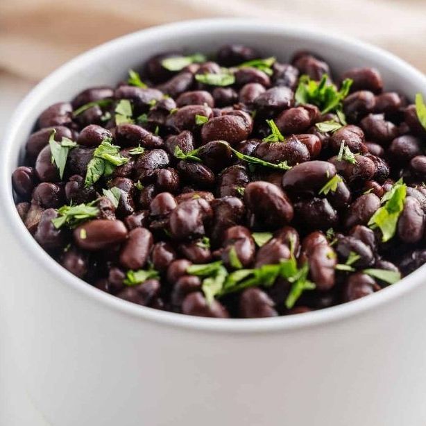 A white bowl filled with black beans and parsley on a table.