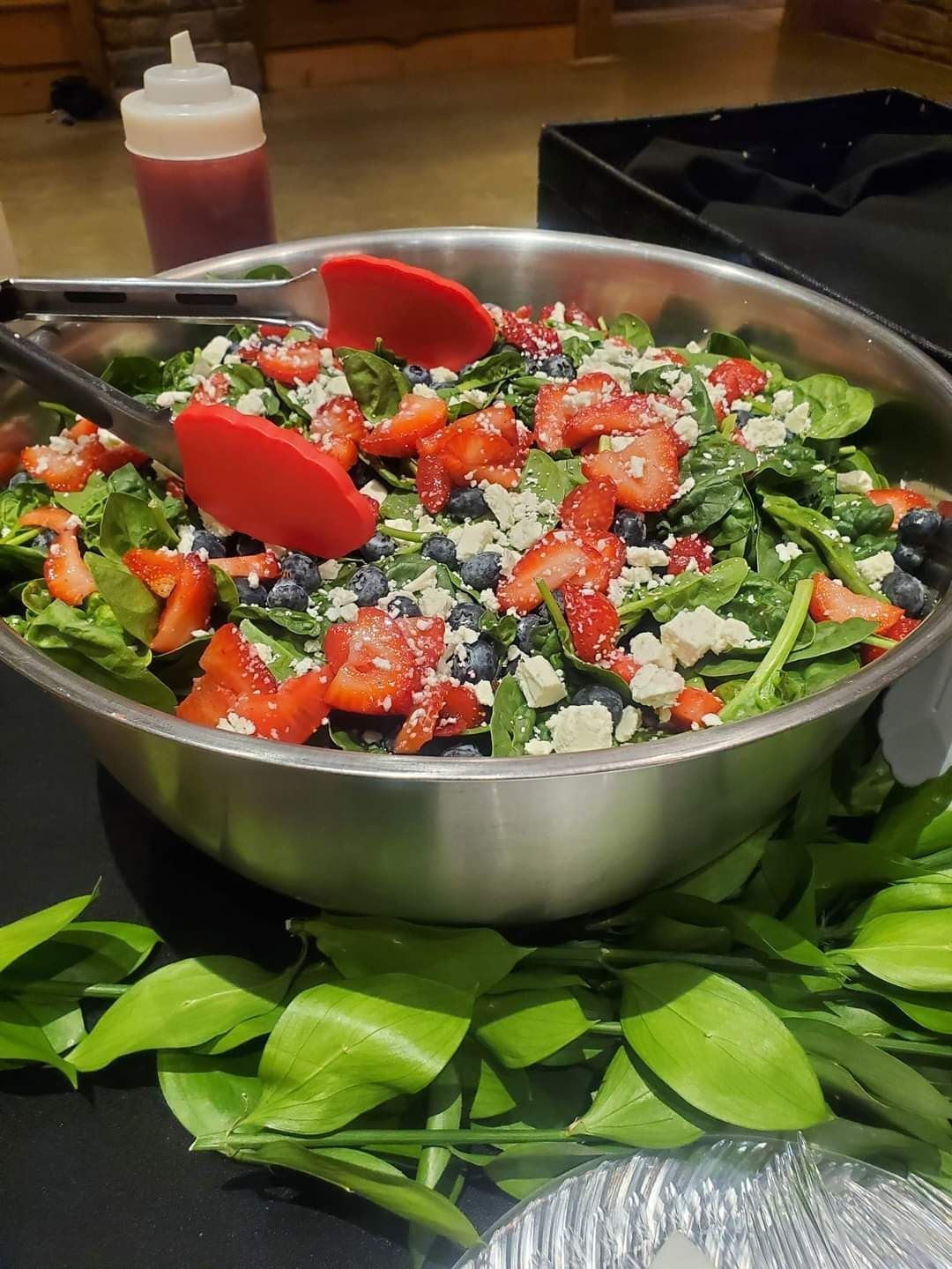 A salad with strawberries, blueberries, spinach, and feta cheese in a metal bowl with tongs