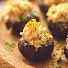 A close up of stuffed mushrooms on a wooden cutting board.