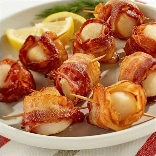 A white plate topped with bacon wrapped scallops on skewers