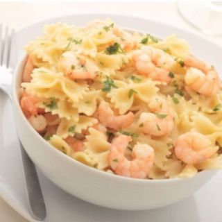 A white bowl filled with pasta and shrimp next to a fork