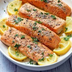 A white plate topped with salmon and lemon slices on a wooden table.