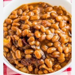 A bowl of baked beans is sitting on a checkered table cloth.