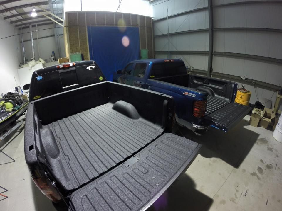 Two trucks are parked in a garage with their trunks open.