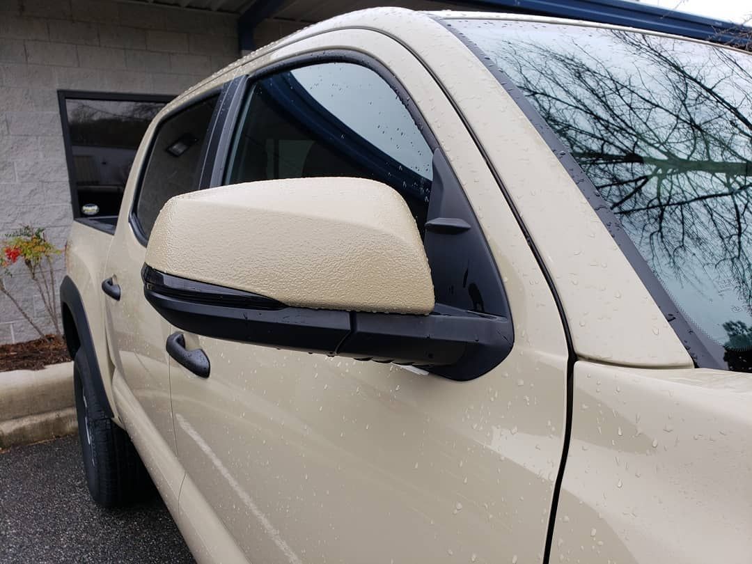 A white truck with black side mirrors is parked in front of a building.