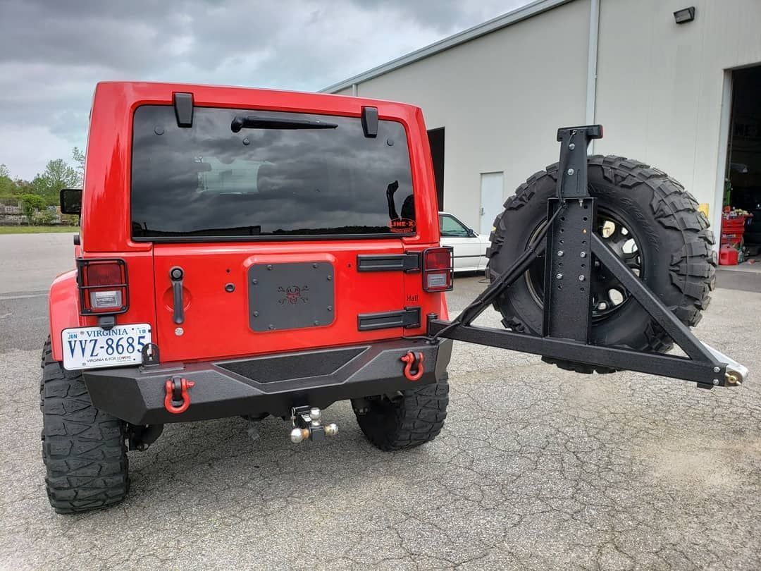A red jeep with a trailer attached to it is parked in front of a building.