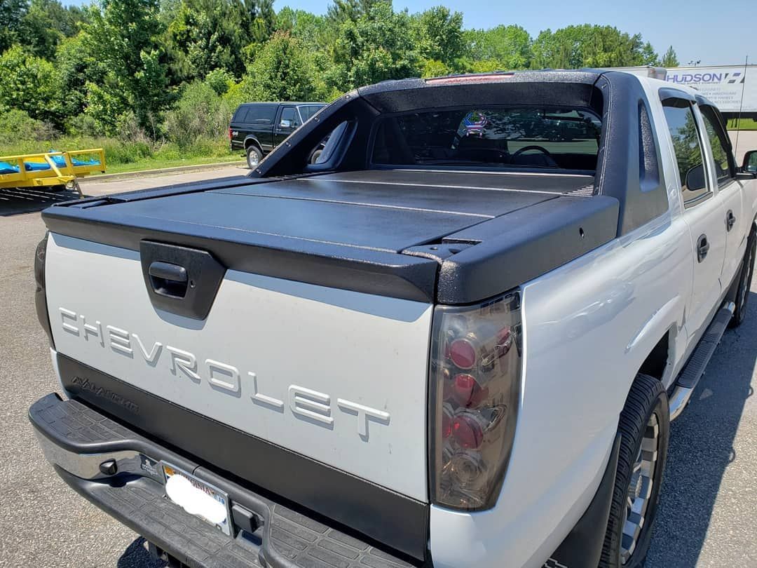 A white truck with a black bed cover is parked on the side of the road.