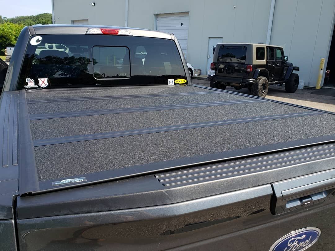A ford truck with a black bed cover is parked in front of a building.
