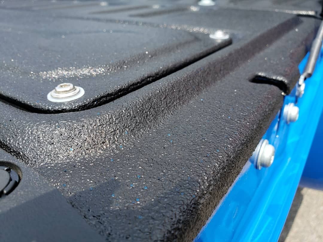 A close up of a blue truck bed with a black cover and screws.