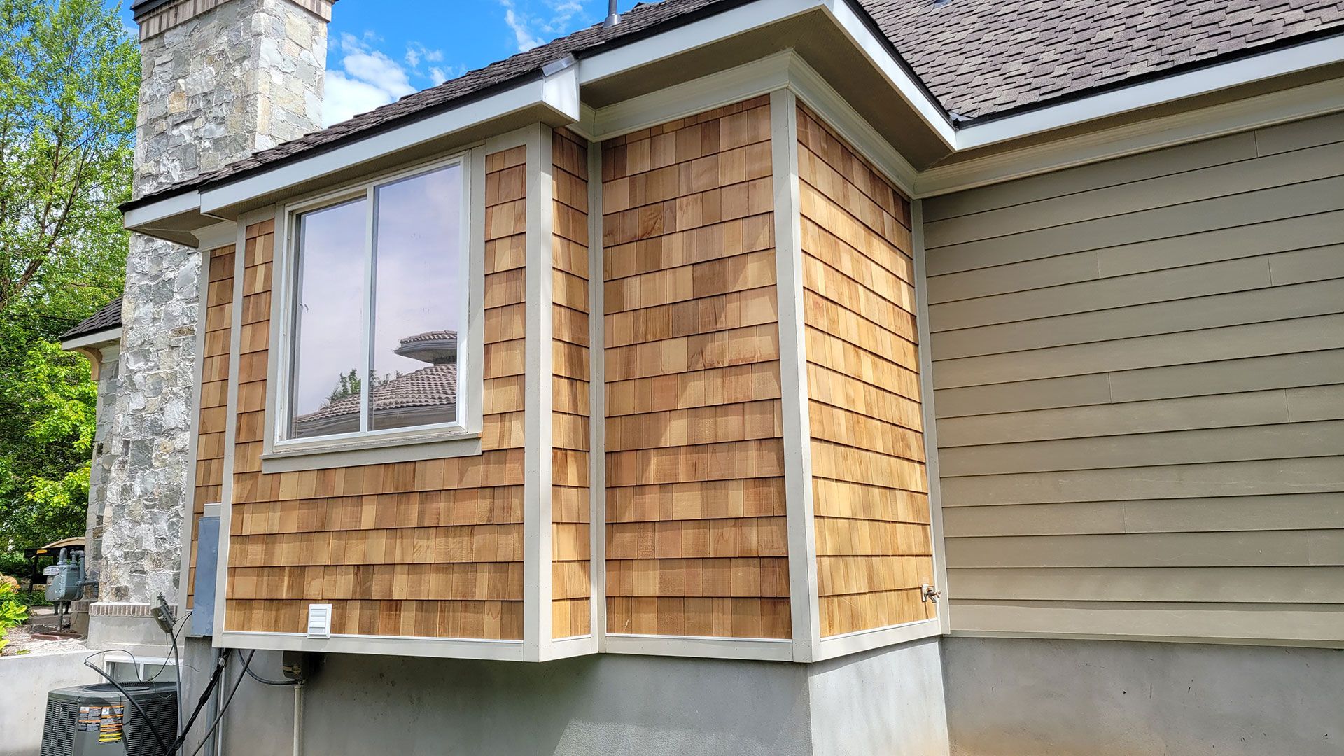 A house exterior with cedar shake siding around a window and beige siding.