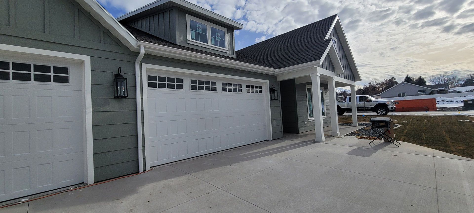 A gray-green house with white garage doors and a gray roof. A driveway is in front.