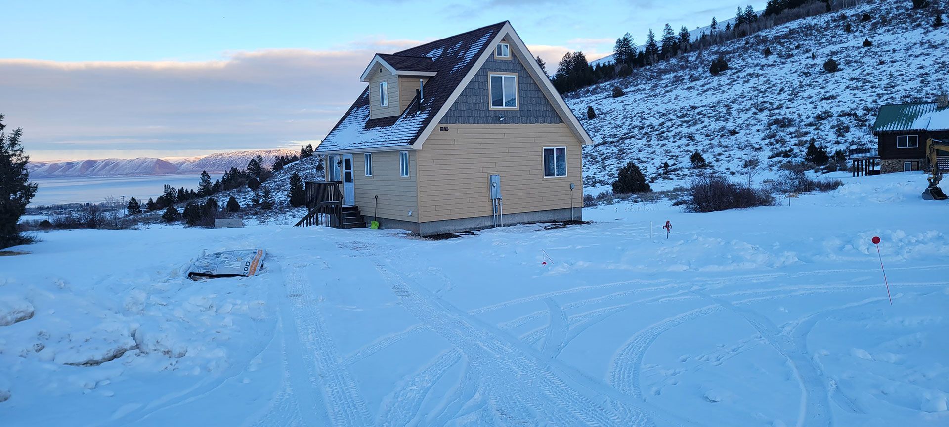 A two-story house with a snow-covered yard and mountain in the background.