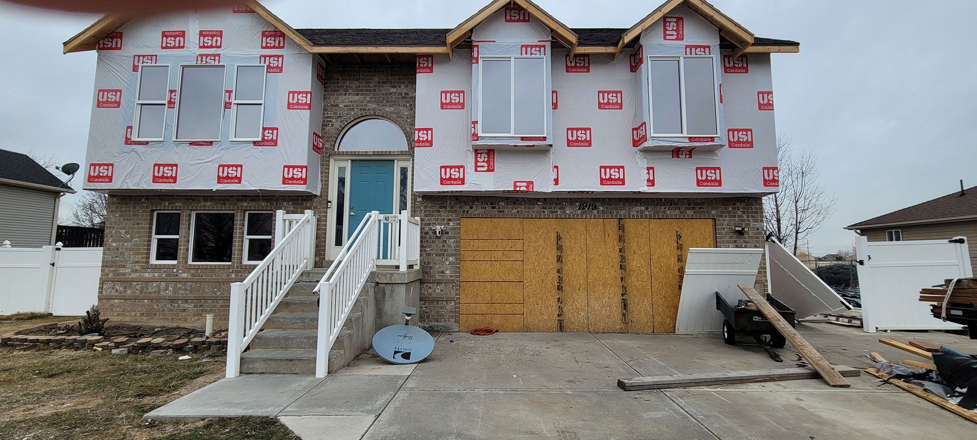 House under construction with brick exterior, plywood garage door, and white trim, cloudy sky.