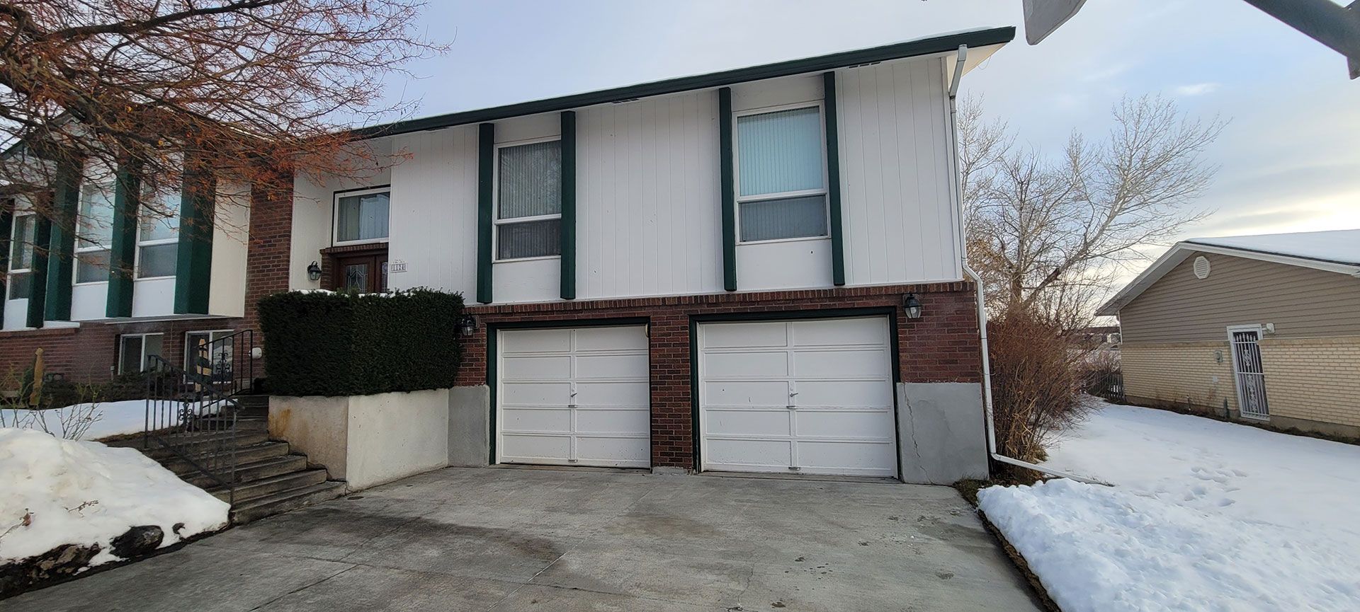 White two-story house with two-car garage in a snowy setting. Brick and white siding. Overcast sky.