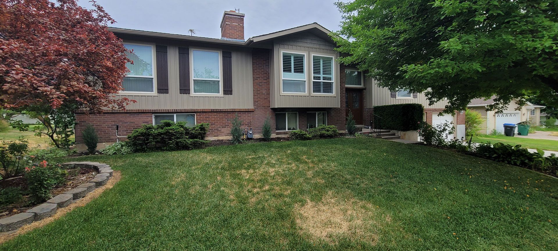 House exterior with red brick and brown siding, front lawn, tree and shrubbery.