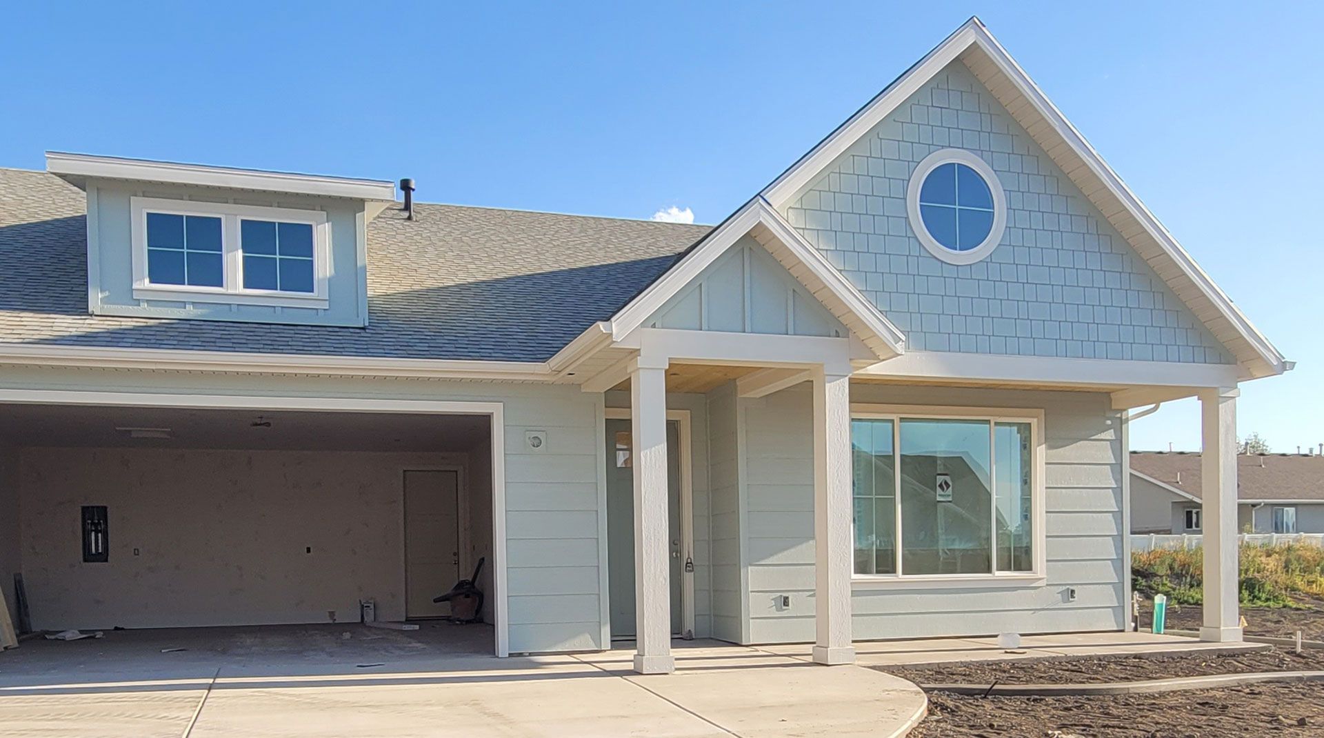 Light blue house with a garage, front porch, and dormer under a clear sky.