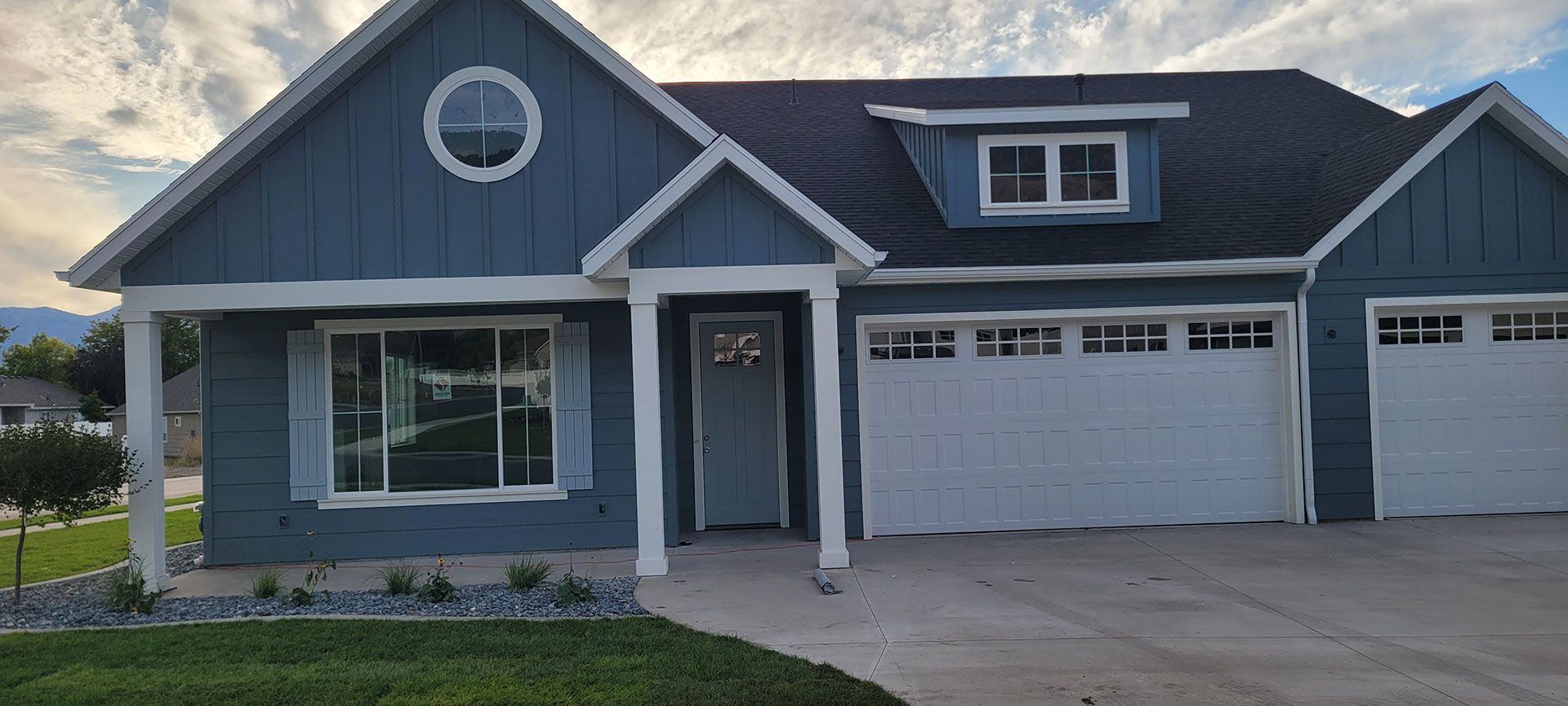 Blue house with white trim, a round window, and two garage doors.