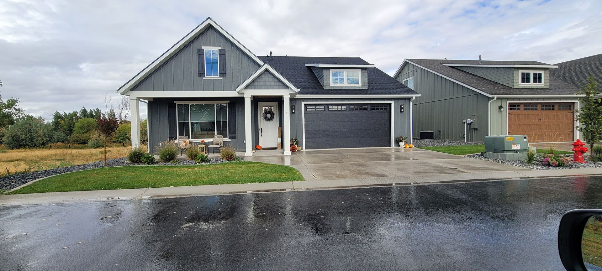 Gray house with black roof and a matching garage. Wet asphalt in front.
