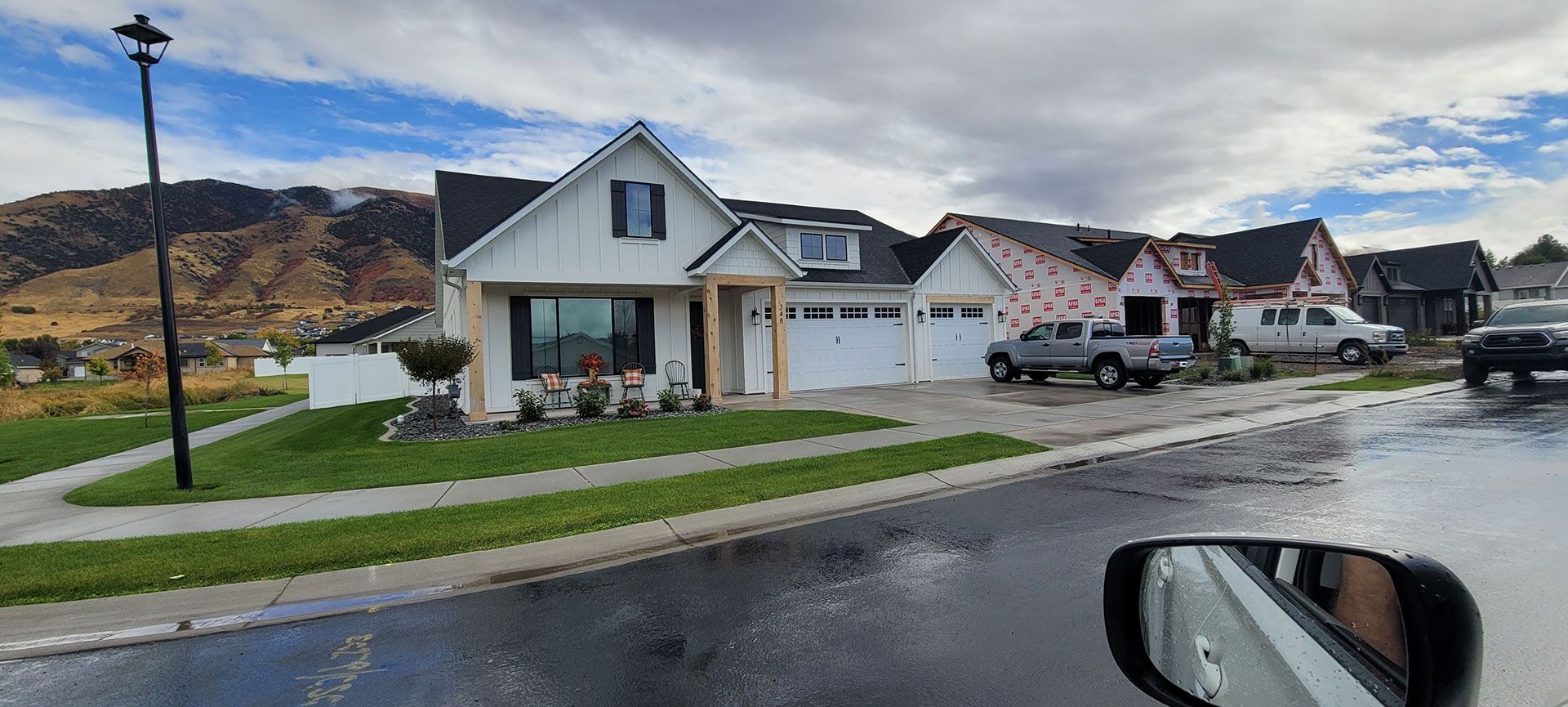 Houses in a suburban neighborhood with construction. Gray sky, wet street, and mountains in the background.