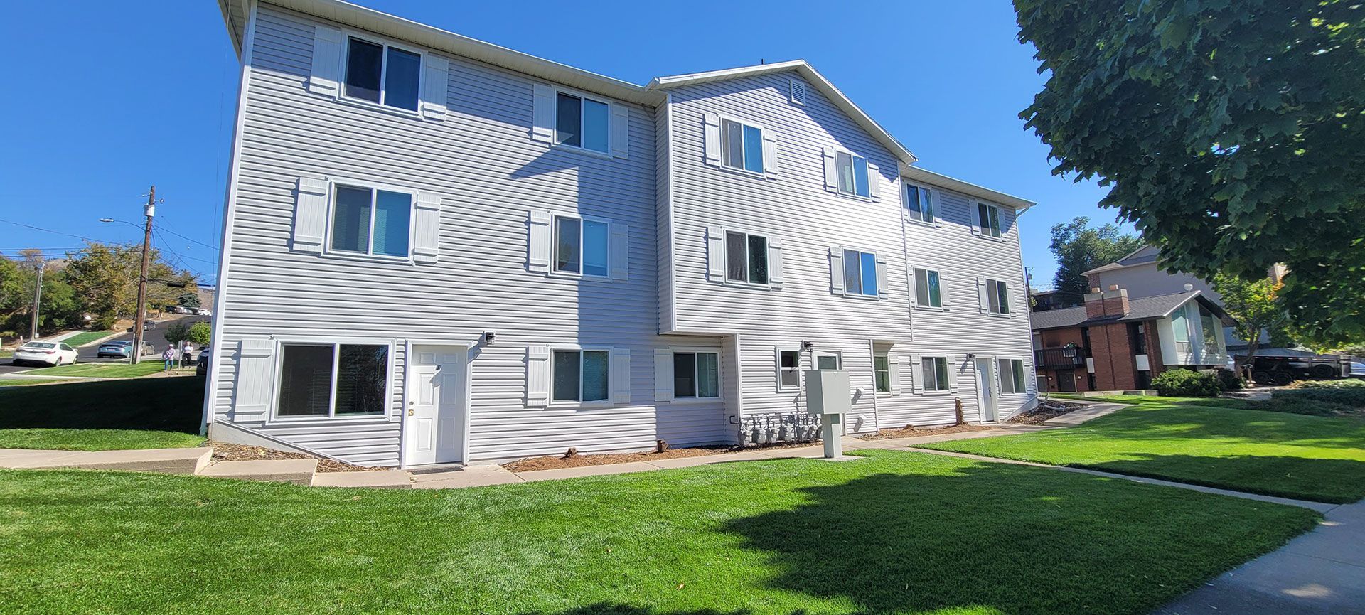 Three-story apartment building with wavy white siding on a green lawn with a blue sky.