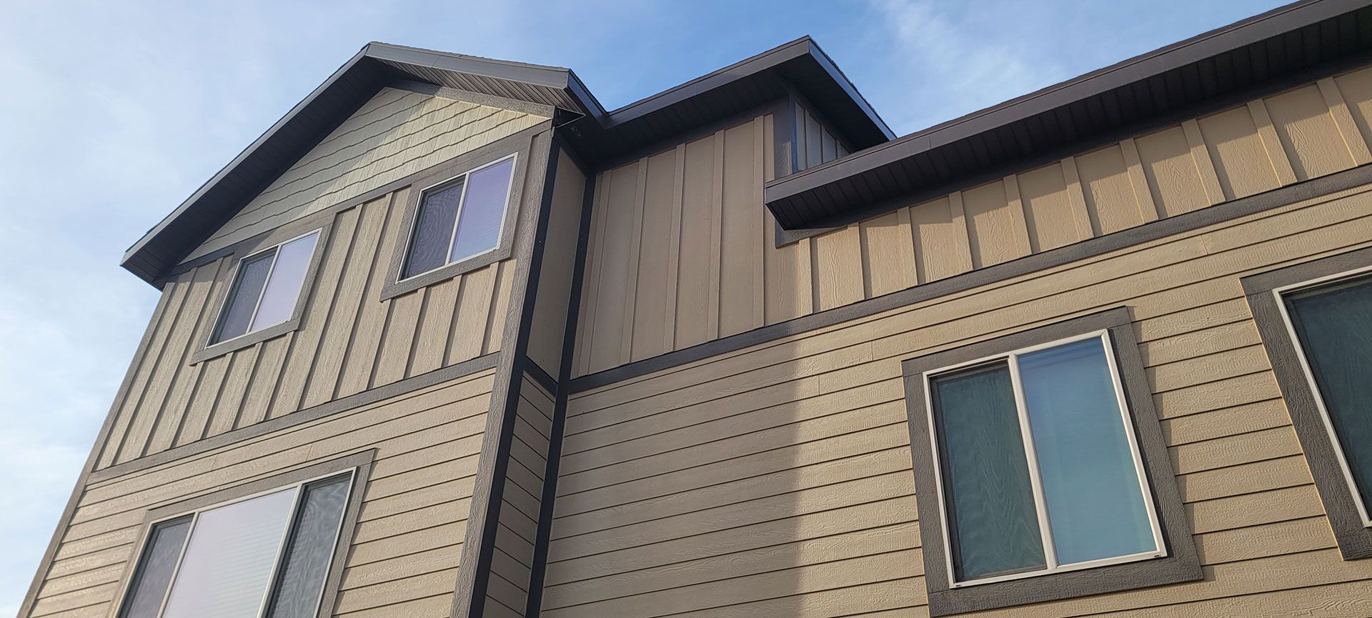 Exterior of a two-story tan and brown building against a blue sky. Windows are visible.