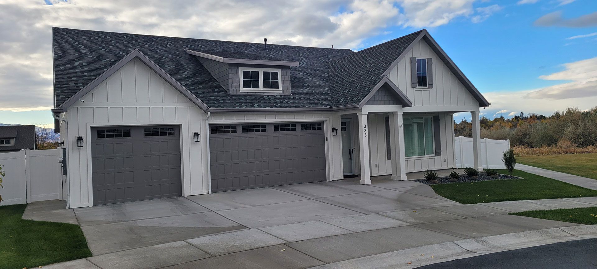 A two-story white house with gray garage doors and a paved driveway under a cloudy sky.