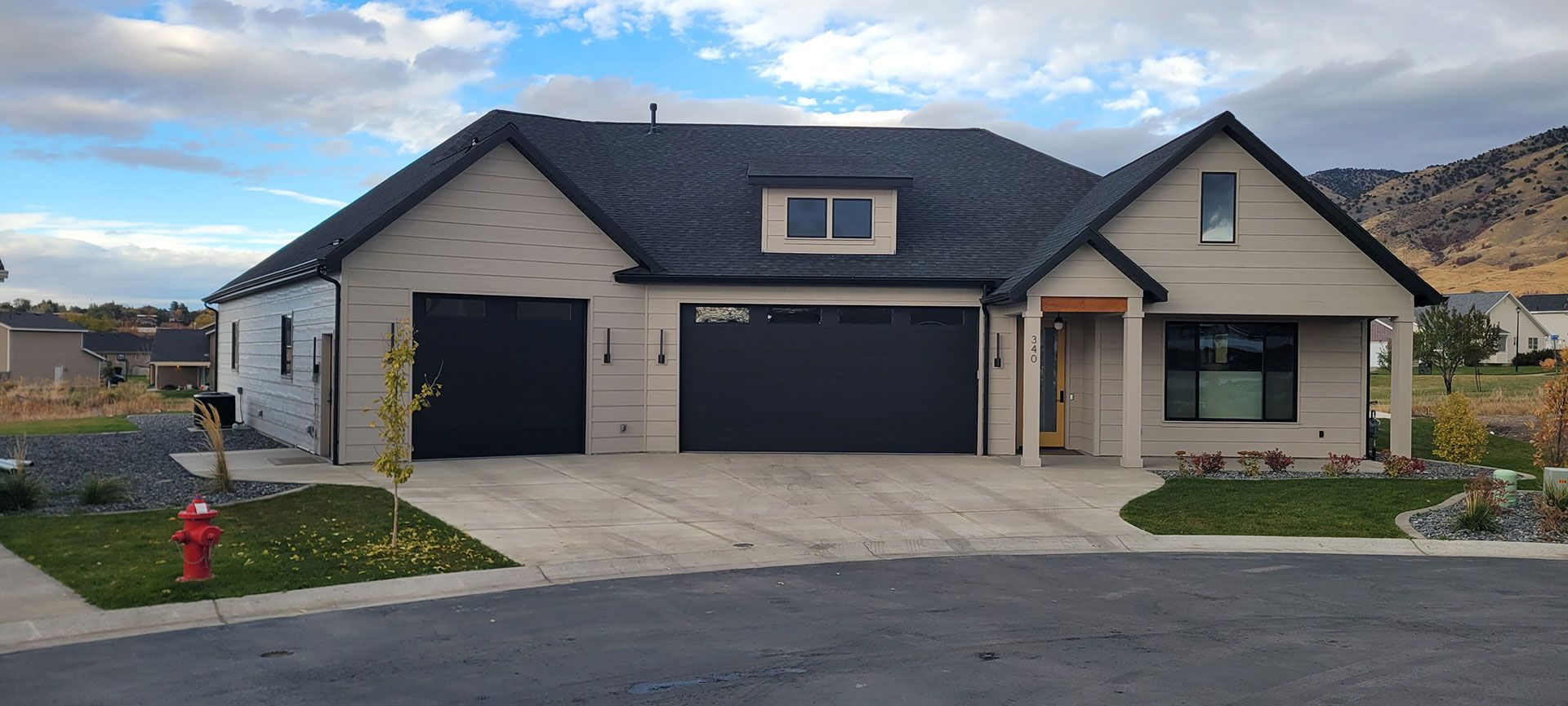 Modern house with black garage doors, grey siding, and a small yard on a cloudy day.
