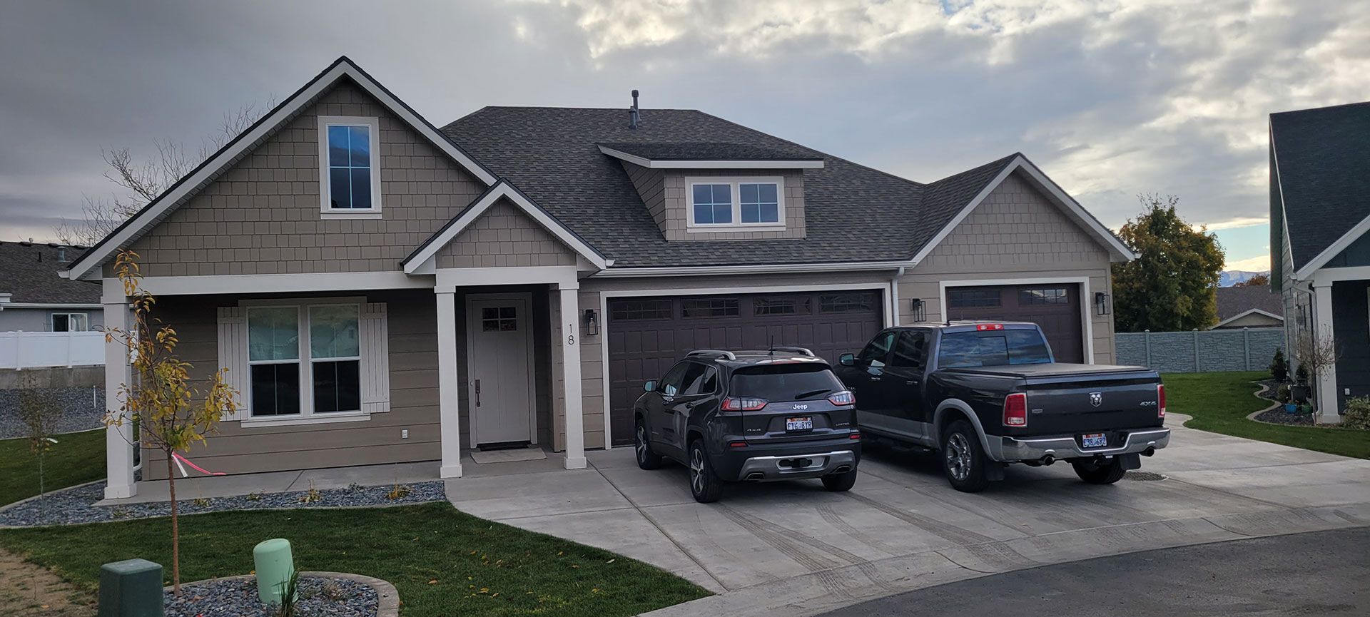 A two-story house with a two-car garage. Two vehicles parked in front. Overcast sky.