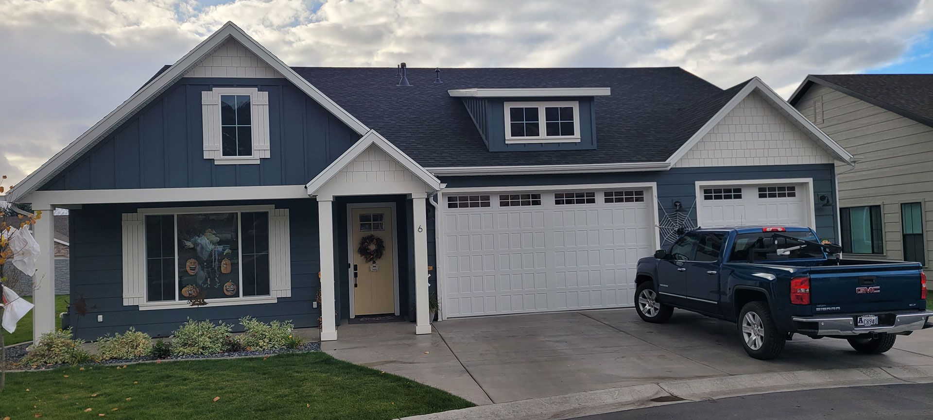 A blue house with white trim, a closed garage, and a parked blue truck on the driveway under a cloudy sky.