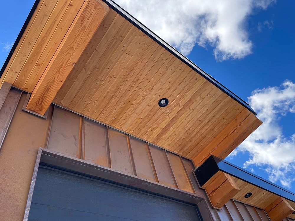 Modern home exterior with wood-paneled soffits, exposed timber rafters, and vertical siding under a bright blue sky.
