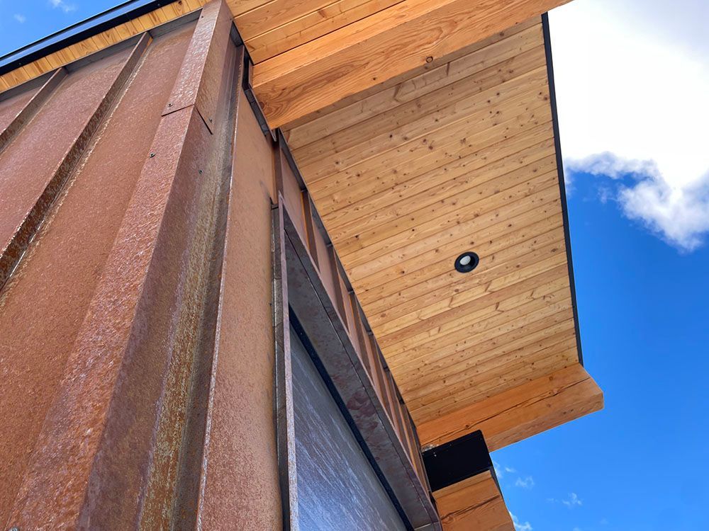 Modern building exterior featuring rusty, vertical steel siding and a light wood-paneled soffit under a roof overhang.
