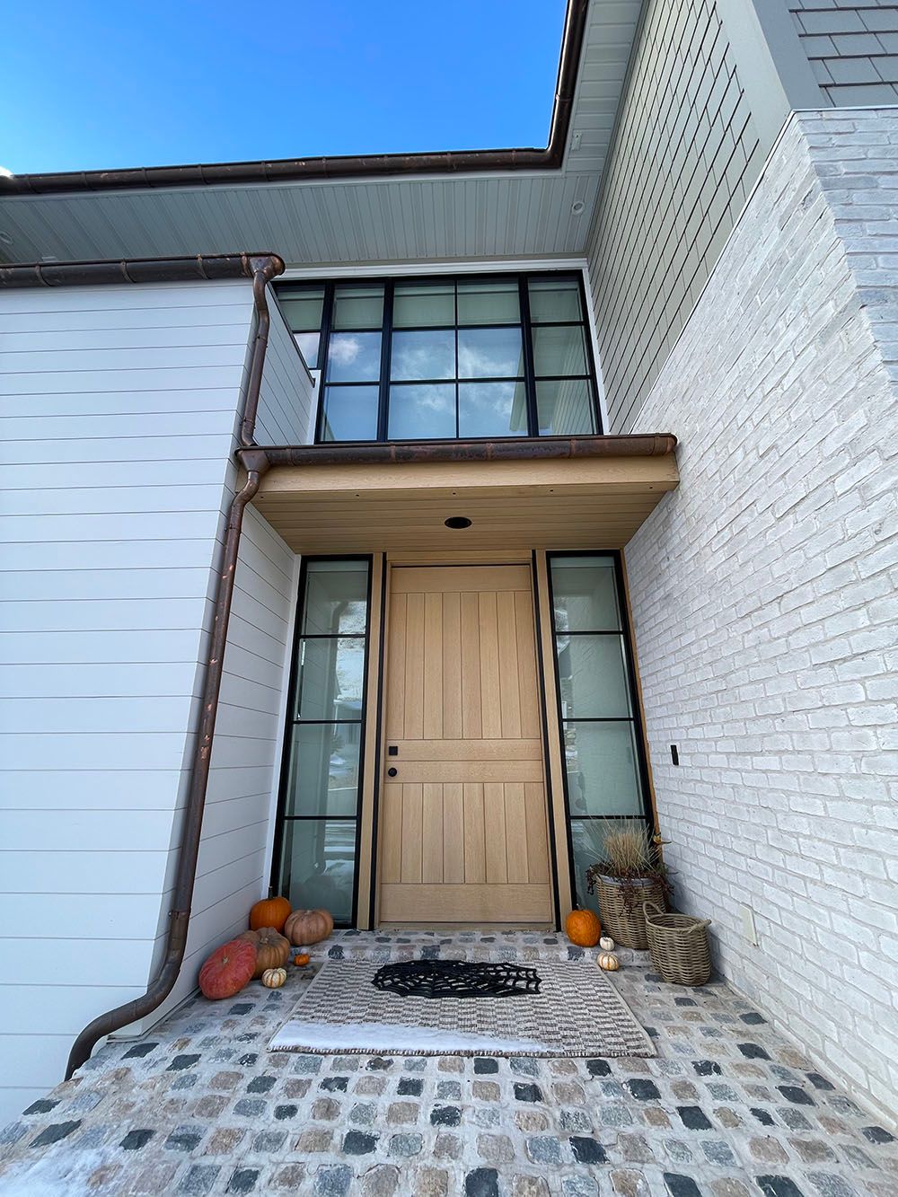 A front entrance with a wooden door, glass side panels, and a large window above, set against white brick and siding.