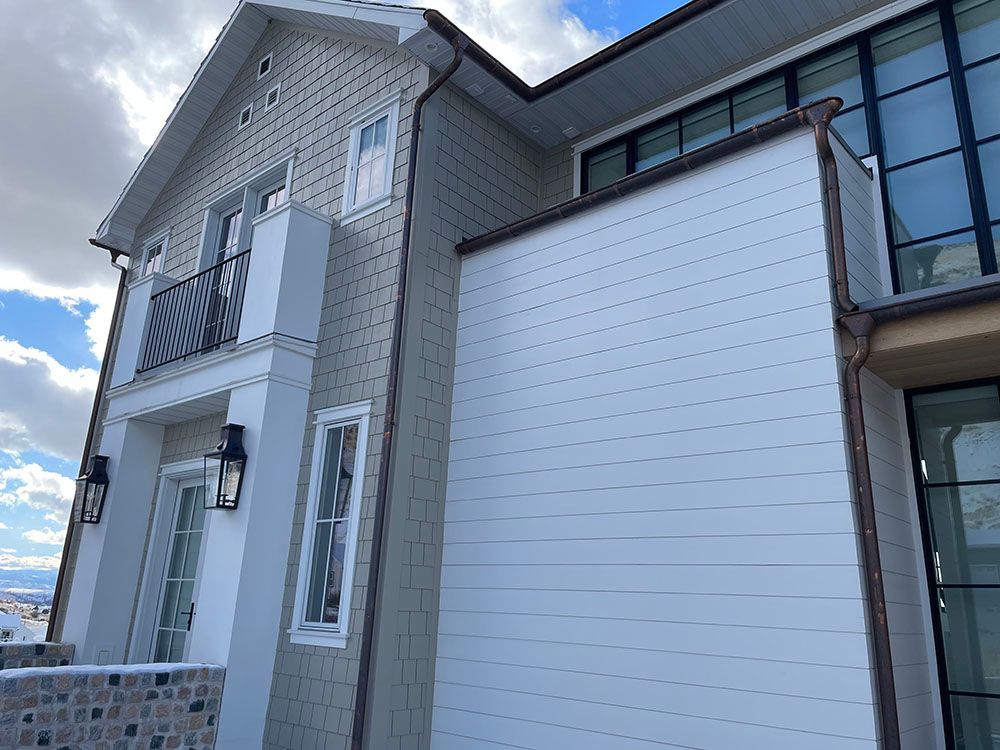 Modern home exterior with a light stone-textured facade, white horizontal siding, a small balcony, and black window frames.