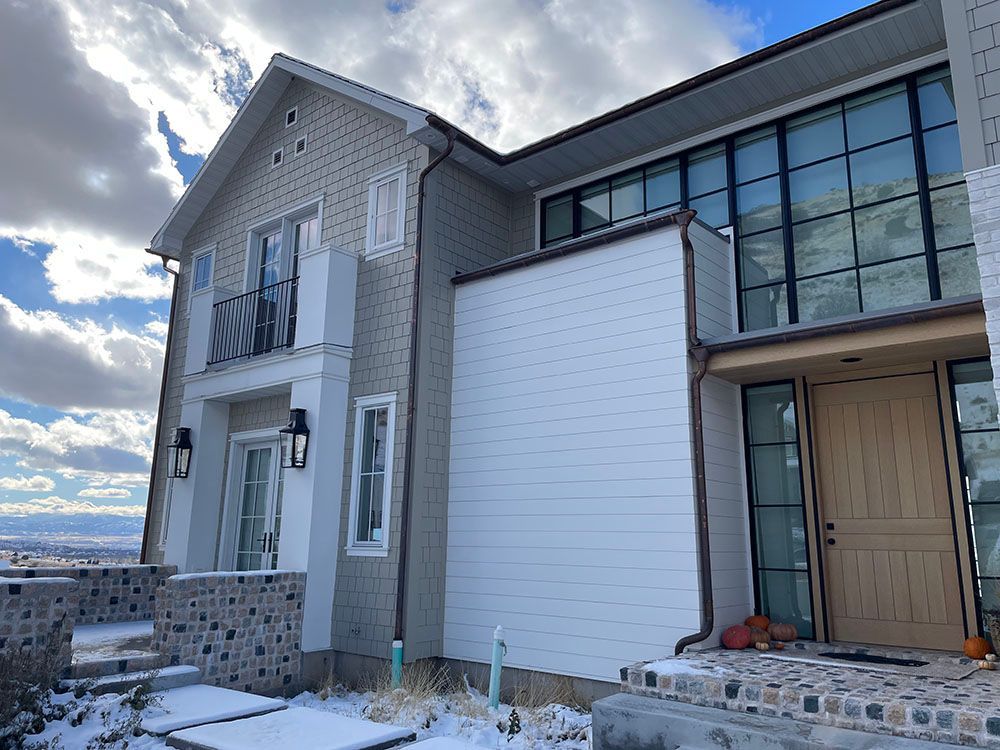 A modern two-story home exterior with white horizontal siding, gray textured walls, and a large black-framed window wall.