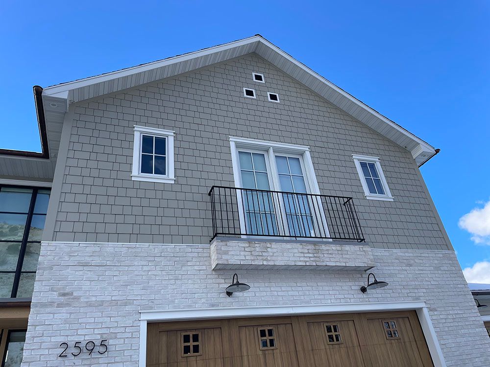 Exterior view of a two-story home with a white brick lower level, grey shingle siding, a balcony, and a garage.