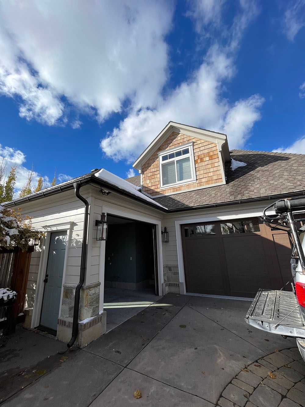 A residential house exterior with a garage and a white door under a bright blue sky with scattered clouds.