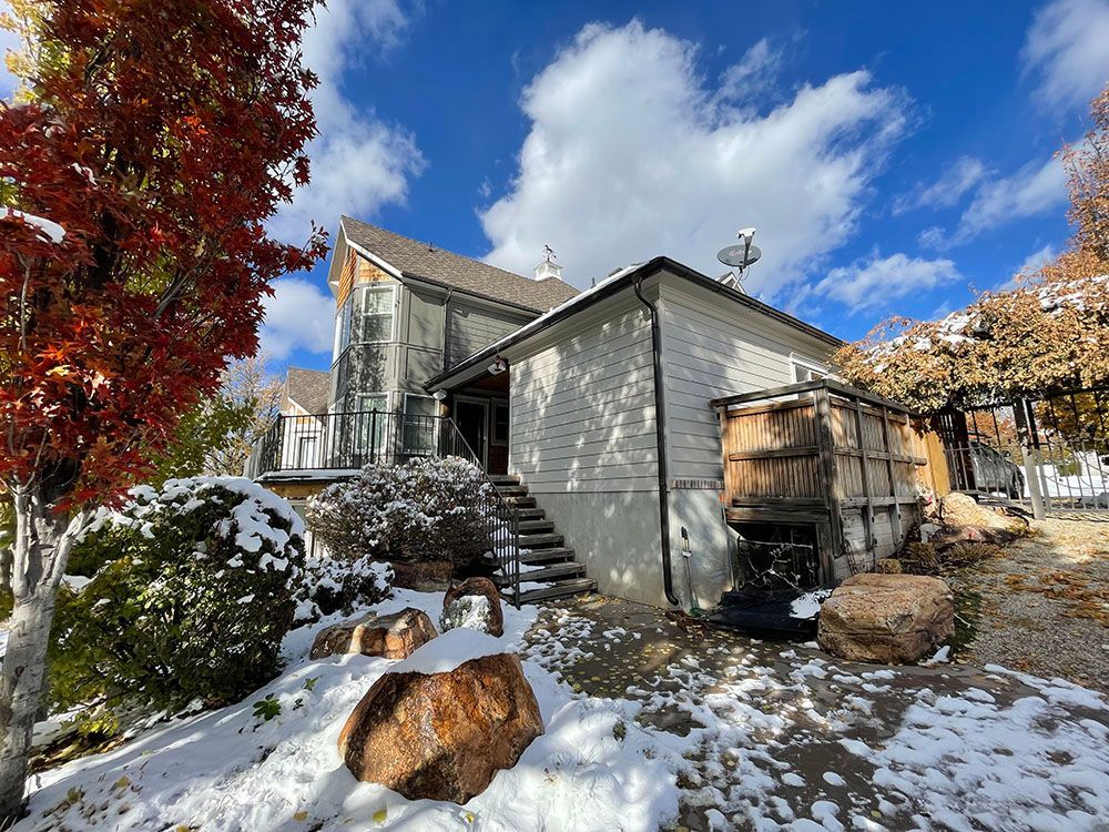 A white home with stone accents and a snowy yard, featuring a vibrant red tree and a blue sky with clouds.