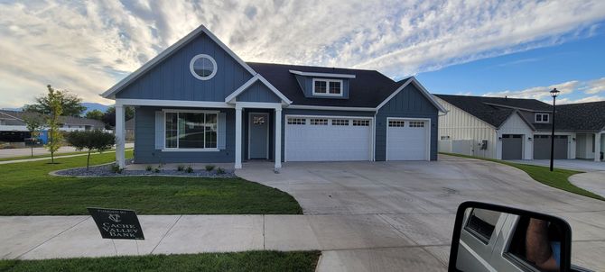 Blue house with white garage doors and a round window in the gable. Green lawn and gray driveway.