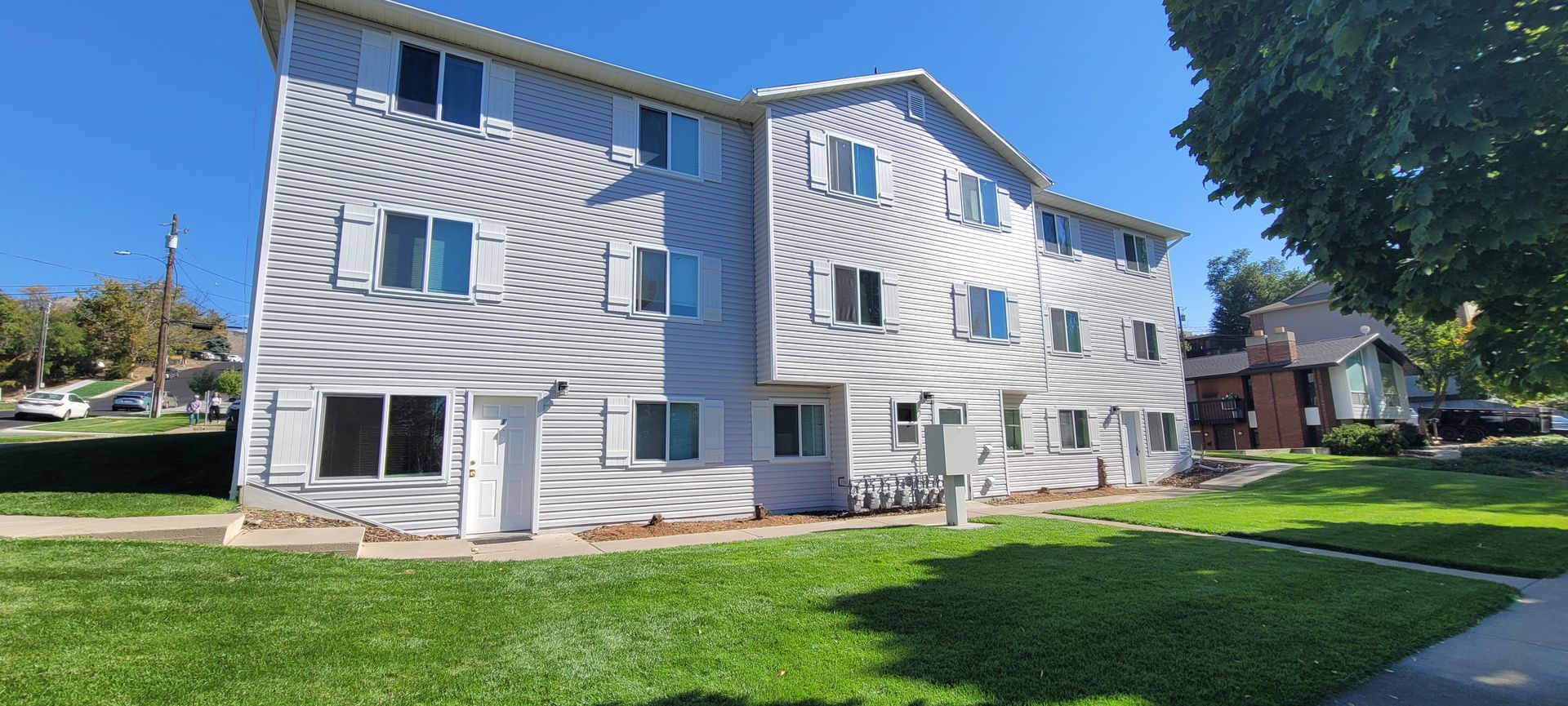 Three-story apartment building with white siding and a green lawn. Clear blue sky.