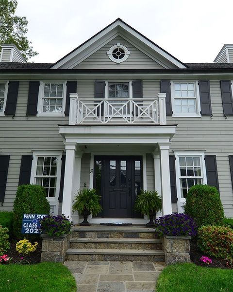 Gray house with white trim, black shutters, front steps, porch with potted plants.