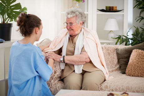 An elderly woman is sitting on a couch talking to a nurse.