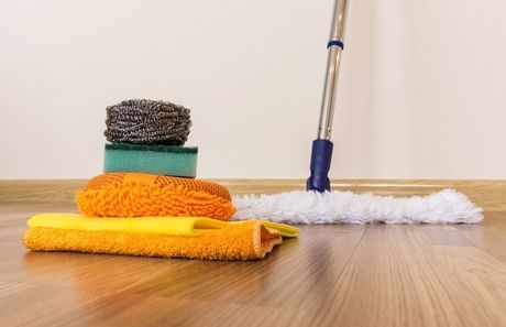 A mop and sponges are sitting on a wooden floor.