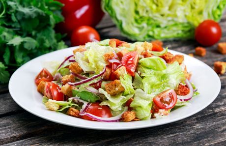 A salad with lettuce , tomatoes , croutons and onions on a white plate on a wooden table.