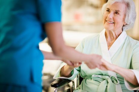 An elderly woman in a wheelchair is shaking hands with a nurse.